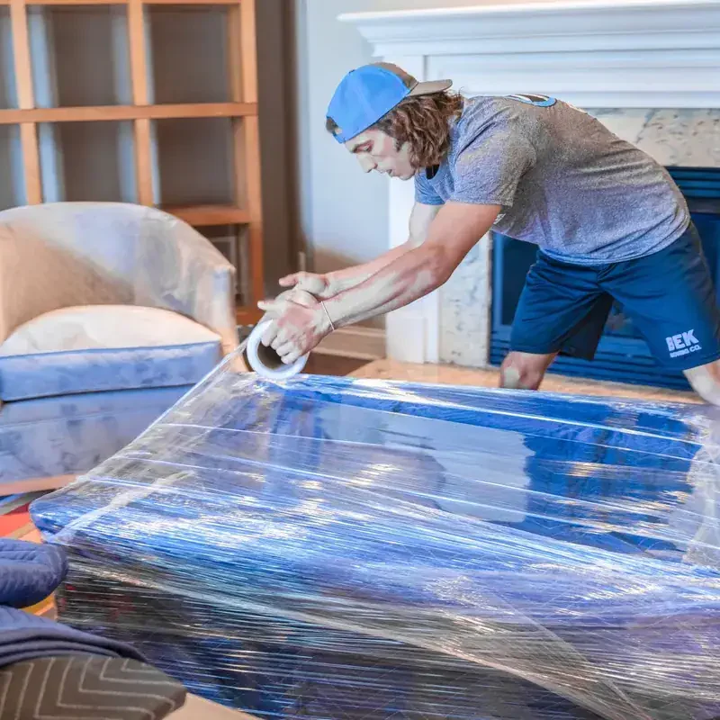 Packing-and-Prep Person wrapping furniture with plastic in a room.