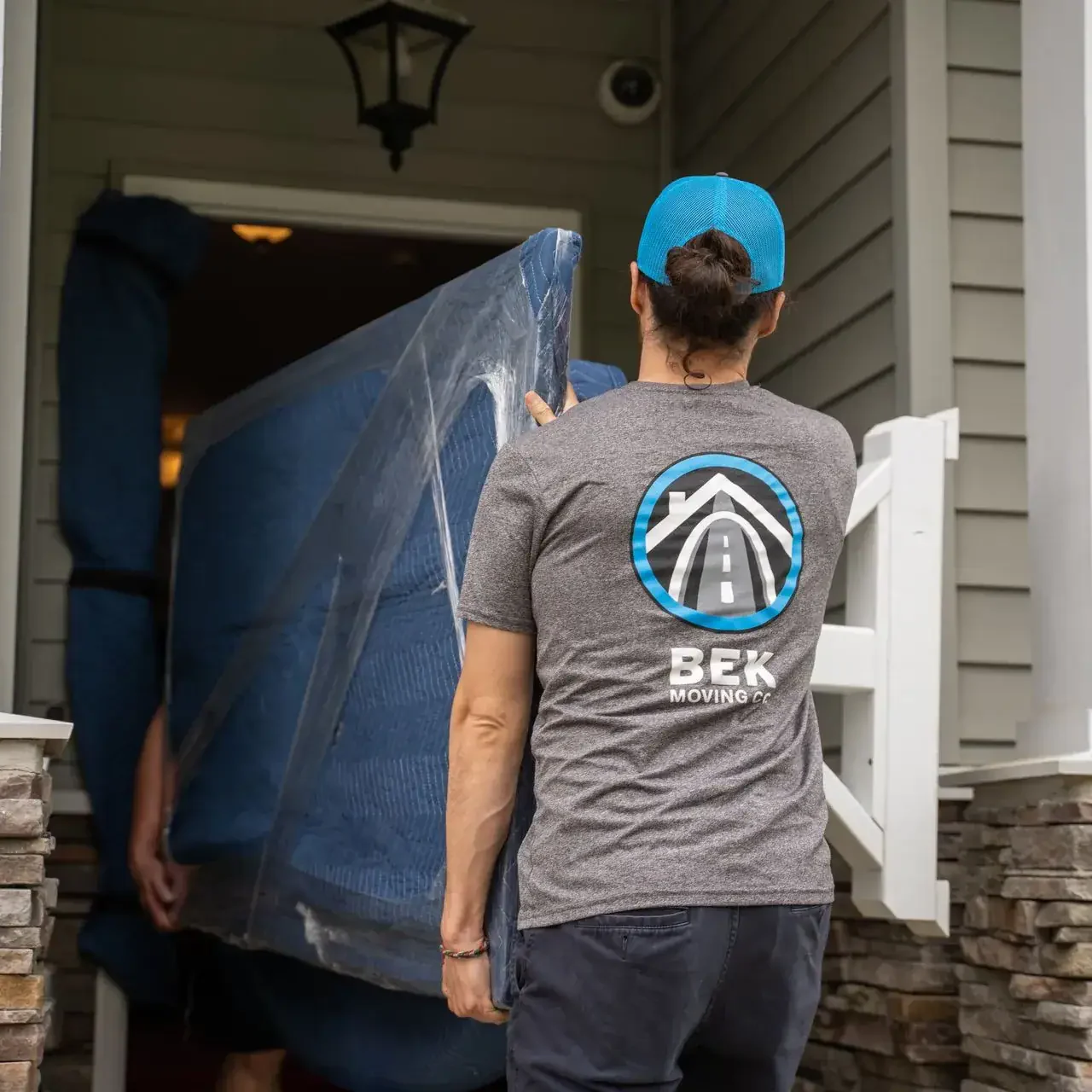 bek-mover-carrying-wrapped-furniture-into-home Mover carrying couch into a house entryway.