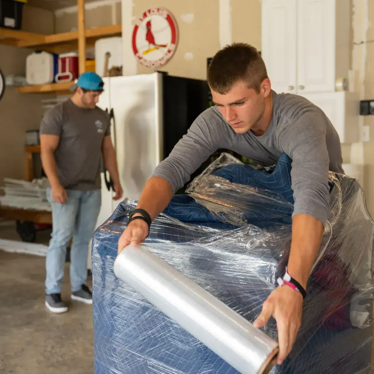 bek-mover-wrapping-furniture-in-garage-with-stretch-wrap Men packing wrapped furniture in the garage.