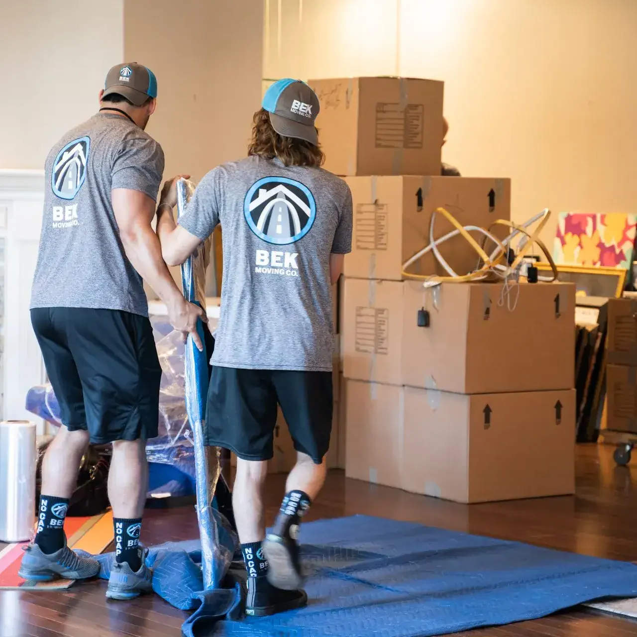 bek-movers-prepping-home-for-move-with-boxes-and-pads Movers packing boxes in a living room.